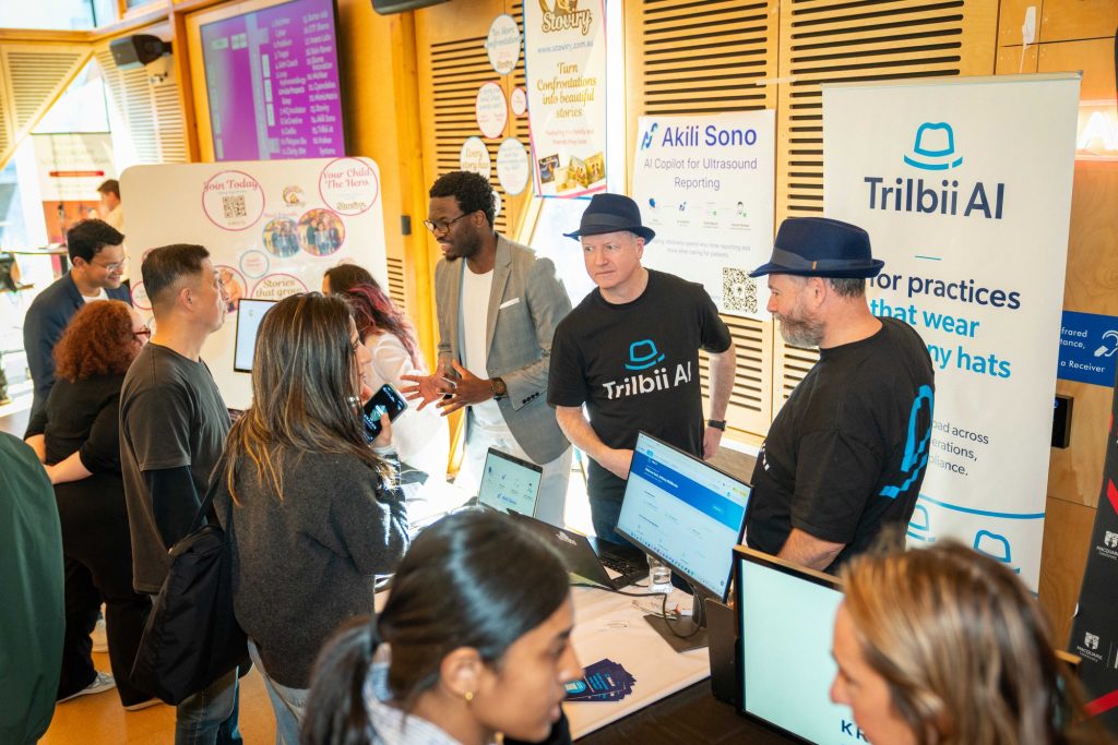 The Trilbii AI stand at Demo Day, team members talking with visitors while the product runs on screens